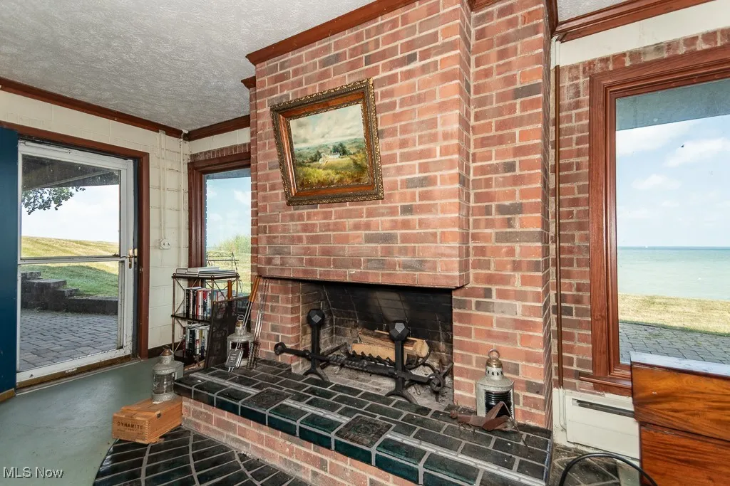Living room featuring crown molding, a textured ceiling, finished concrete flooring, a brick fireplace, and a baseboard radiator
