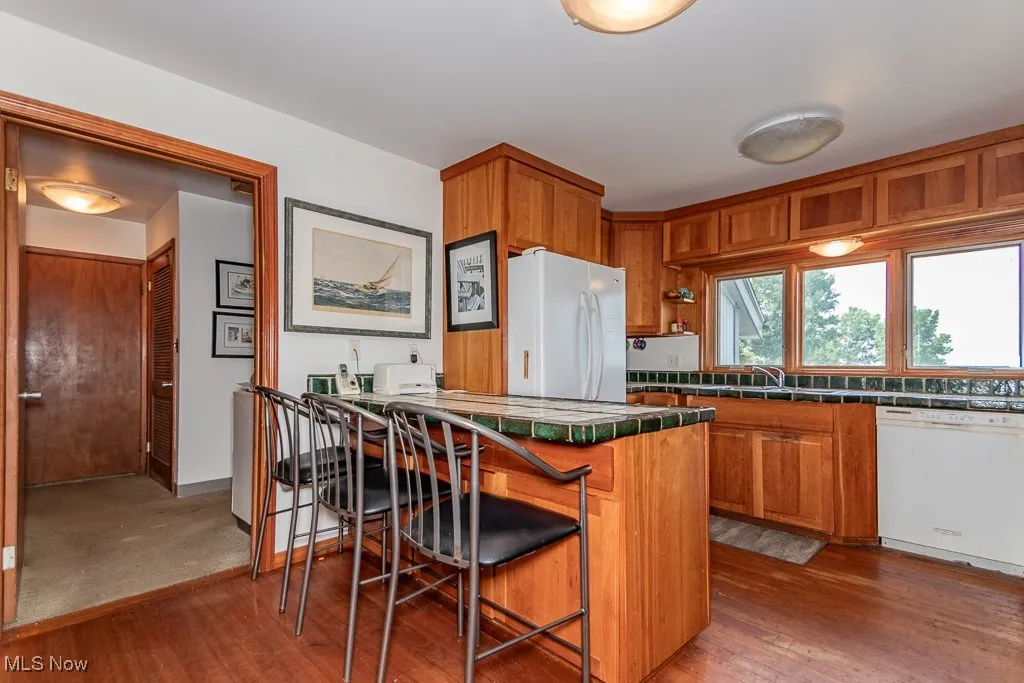 Kitchen with tile countertops, white appliances, brown cabinets, a kitchen bar, and hardwood / wood-style flooring