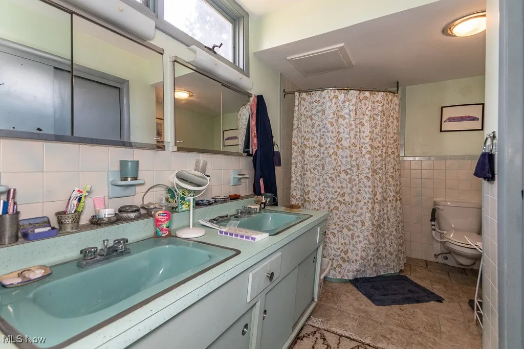 Bathroom featuring tile walls, double vanity, tile patterned flooring, and a shower with curtain