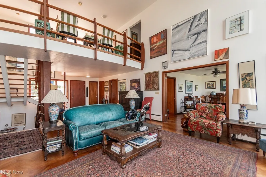 Living room featuring a high ceiling, a ceiling fan, baseboard heating, and wood finished floors