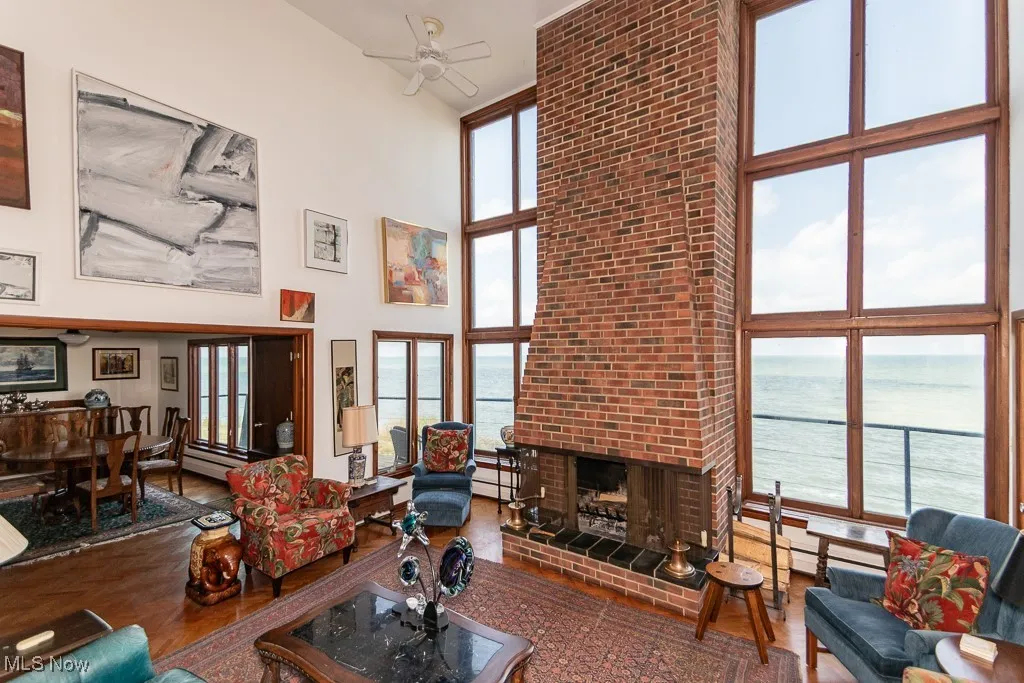 Living room with a towering ceiling, a water view, a ceiling fan, a brick fireplace, and wood finished floors