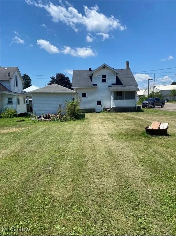 Back of house featuring a chimney, a lawn, and a shingled roof