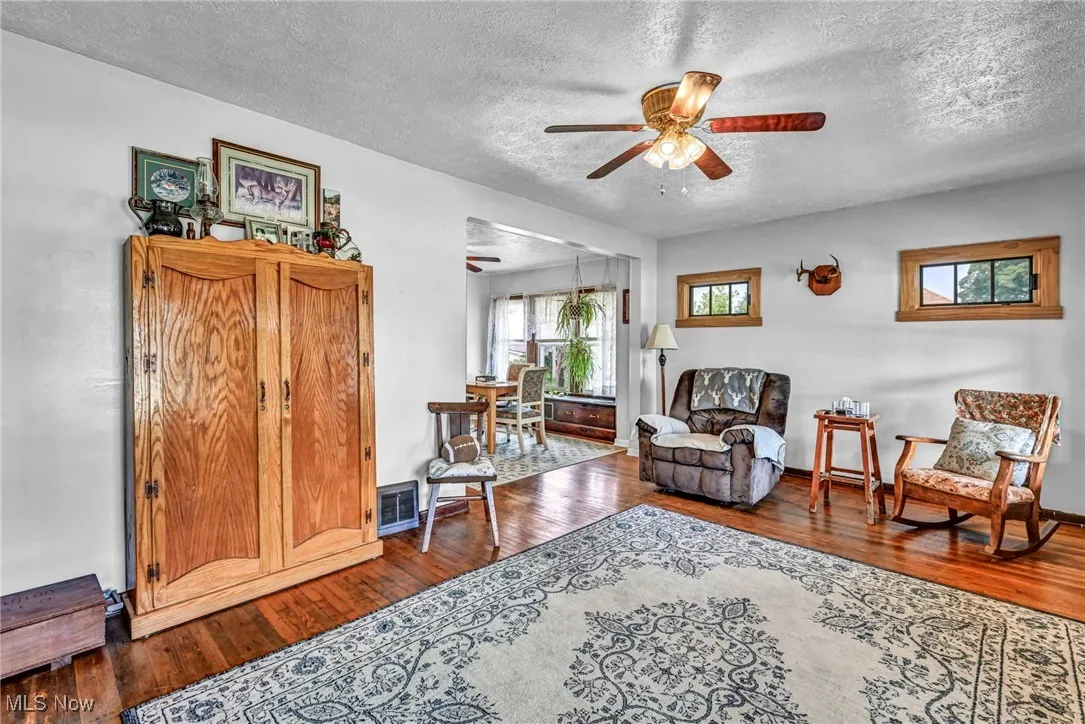 Living area with a ceiling fan, a textured ceiling, and hardwood / wood-style floors