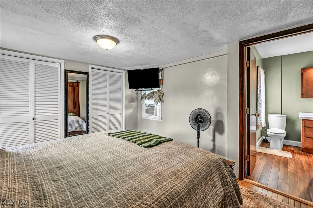 Bedroom featuring wood-type flooring, multiple closets, a textured ceiling, and ensuite bathroom