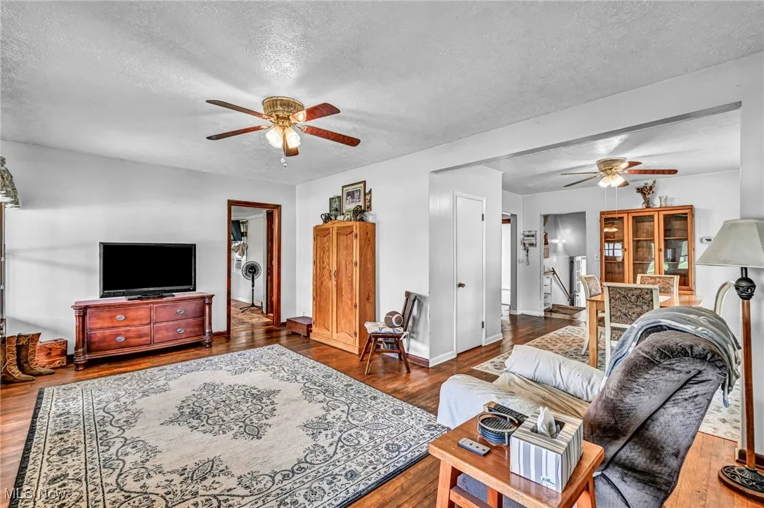 Living room with ceiling fan, a textured ceiling, and wood finished floors