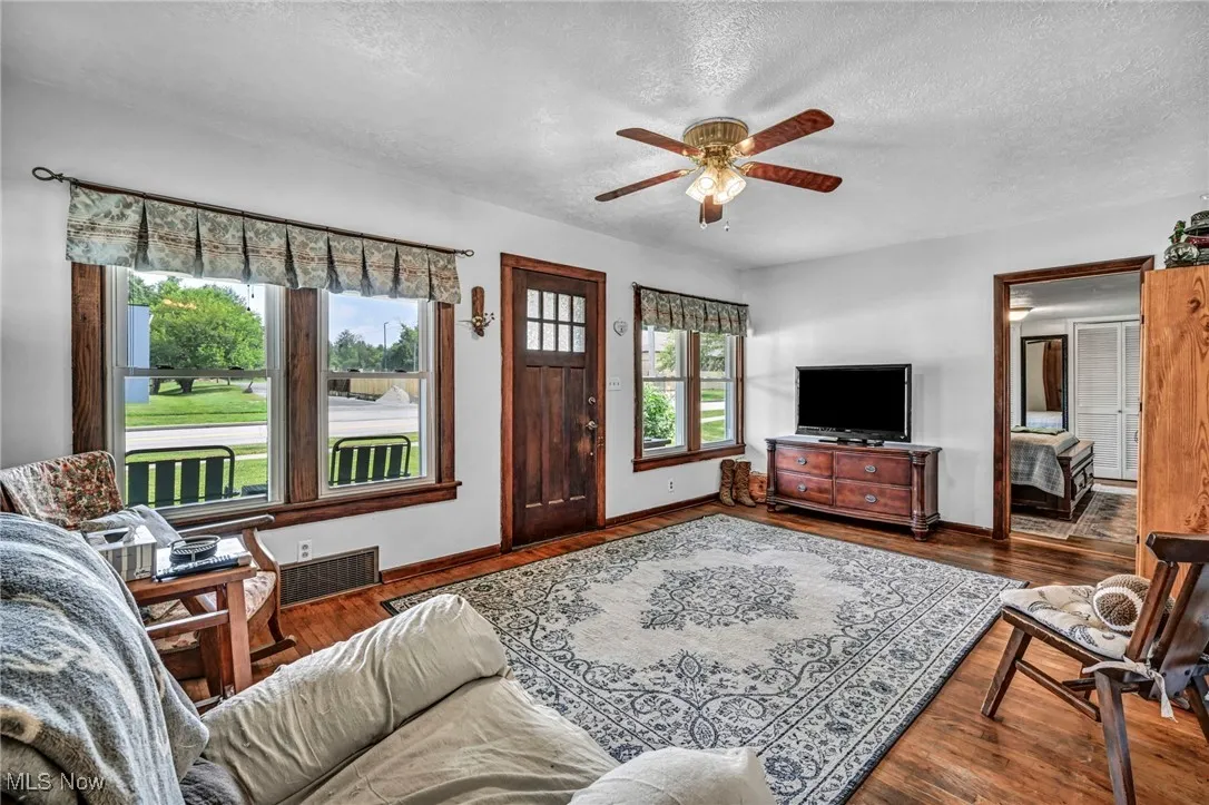 Living room with a textured ceiling, a ceiling fan, and wood finished floors