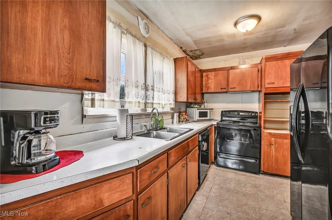 Kitchen with black appliances, light countertops, brown cabinets, and light tile patterned floors