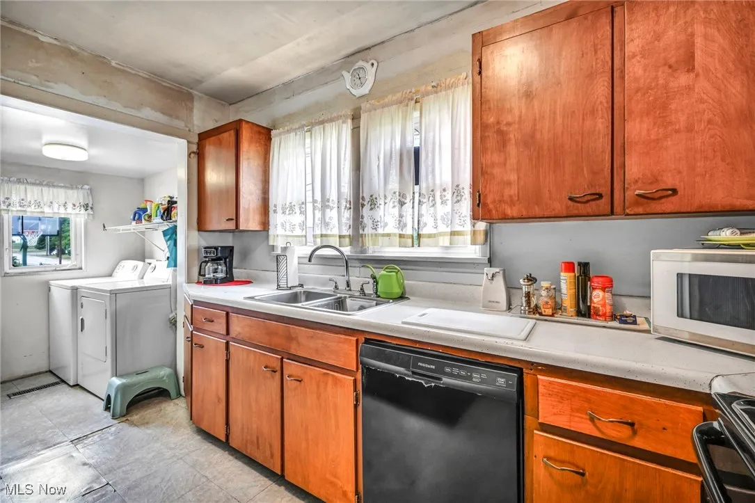 Kitchen featuring washing machine and clothes dryer, black appliances, light countertops, and brown cabinetry