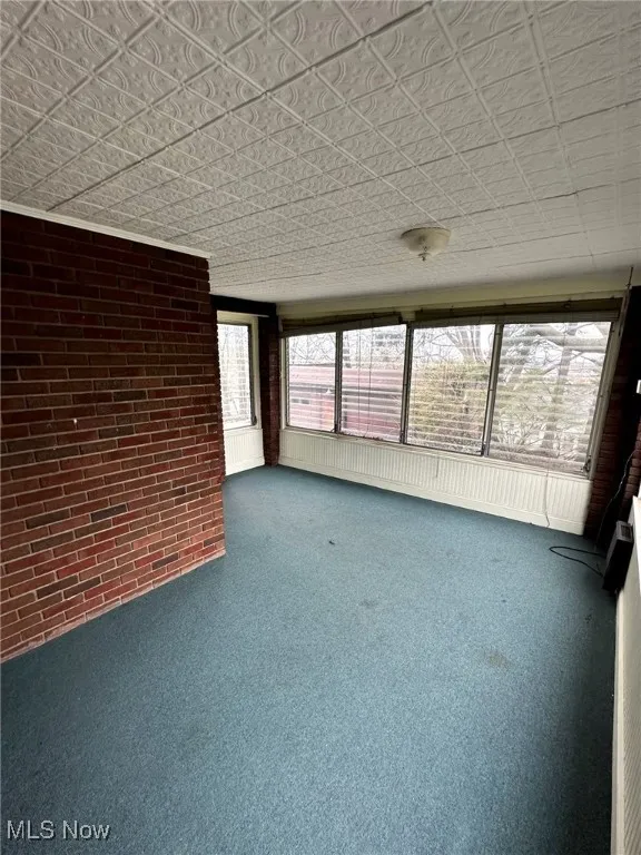 Unfurnished sunroom featuring carpet floors and brick wall