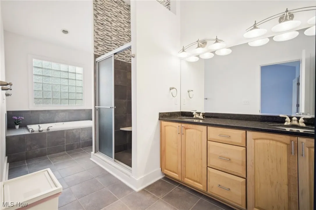 Bathroom featuring tile patterned floors, a shower stall, double vanity, and a garden tub
