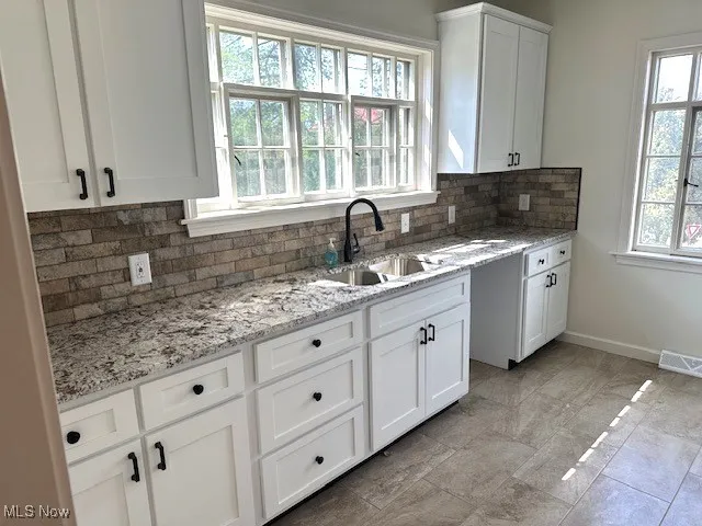 Kitchen featuring white cabinetry, backsplash, and light stone countertops