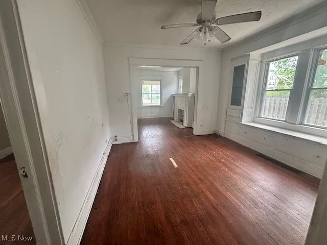 Unfurnished living room with crown molding, a ceiling fan, and dark wood-style flooring