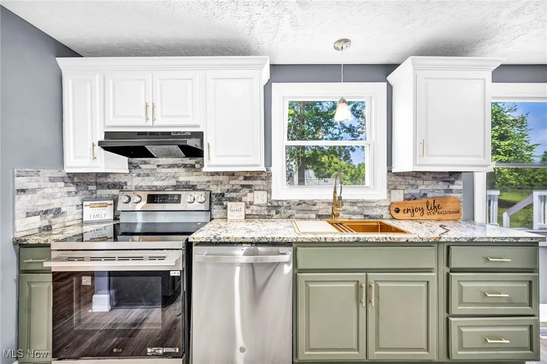 Kitchen featuring green cabinets, appliances with stainless steel finishes, decorative backsplash, ventilation hood, and white cabinetry