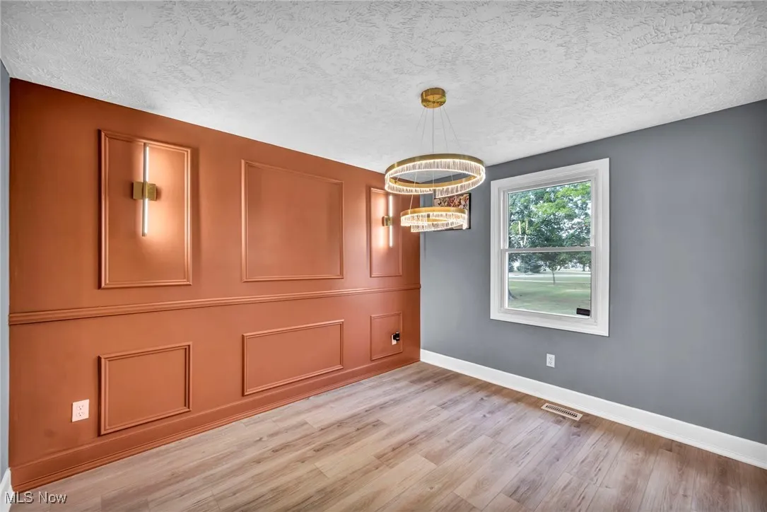 Unfurnished room featuring a chandelier, light wood-style flooring, and a textured ceiling