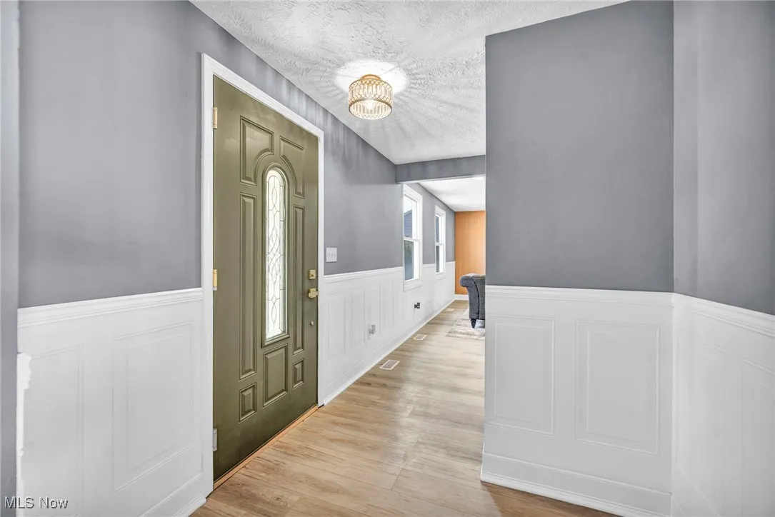 Entryway featuring wainscoting, a decorative wall, a textured ceiling, light wood-style floors, and a chandelier