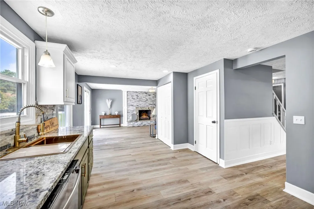 Kitchen featuring a fireplace, a textured ceiling, light wood-style flooring, light stone countertops, and stainless steel dishwasher