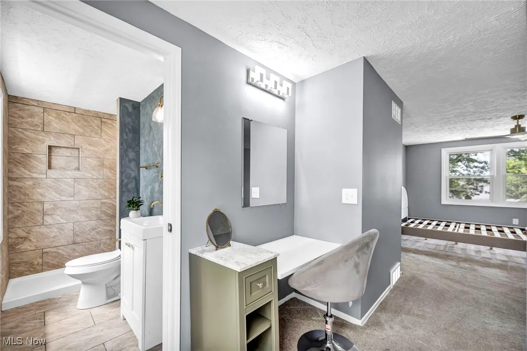 Full bath featuring a textured ceiling, a tile shower, and vanity