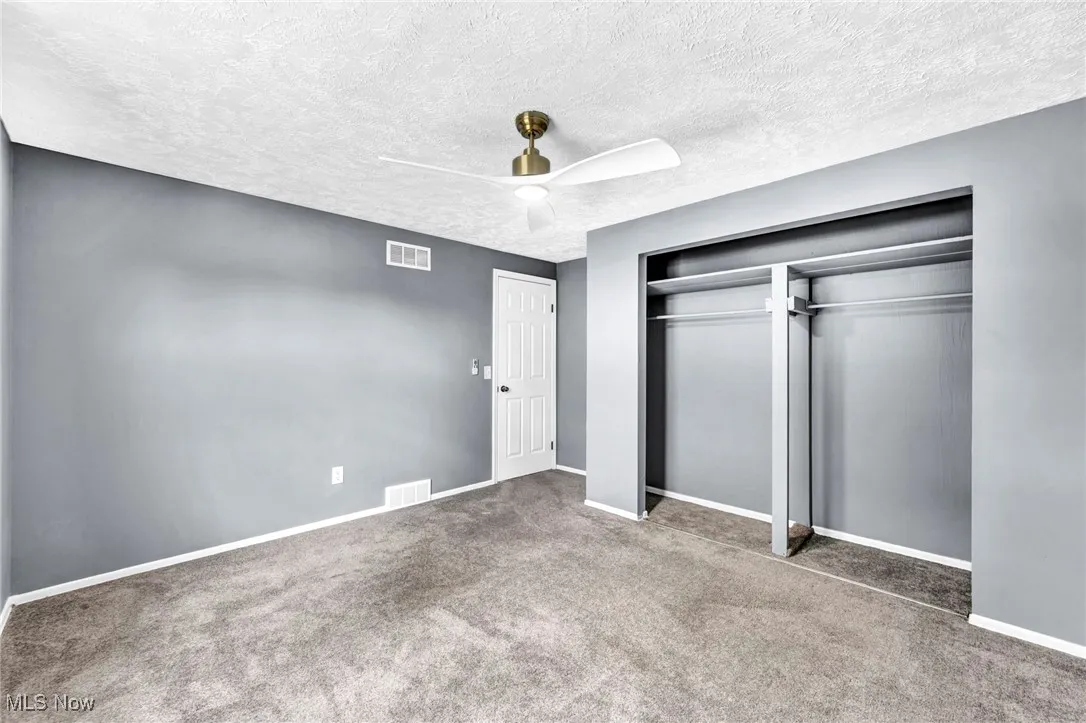 Unfurnished bedroom with a textured ceiling, carpet flooring, a closet, and a ceiling fan