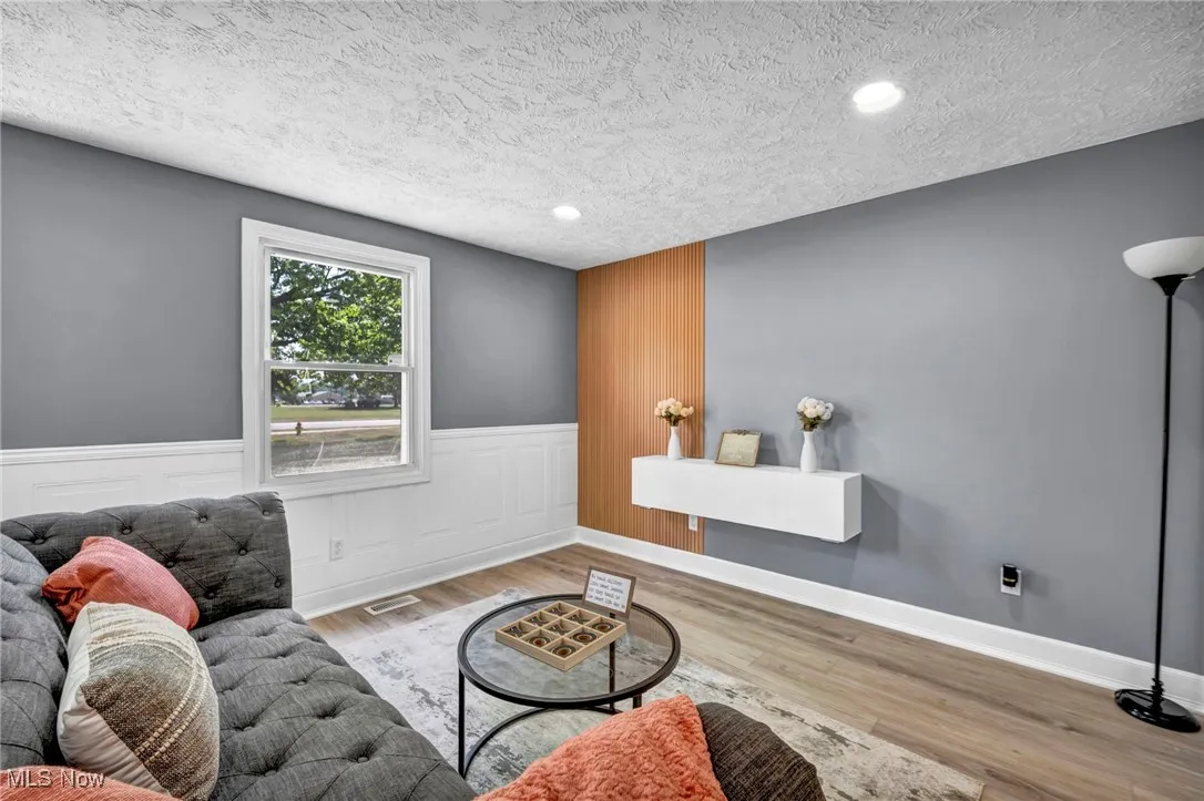 Living room with wainscoting, a textured ceiling, wood finished floors, and recessed lighting