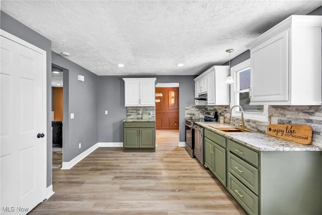 Kitchen with green cabinets, white cabinets, appliances with stainless steel finishes, decorative backsplash, and a textured ceiling