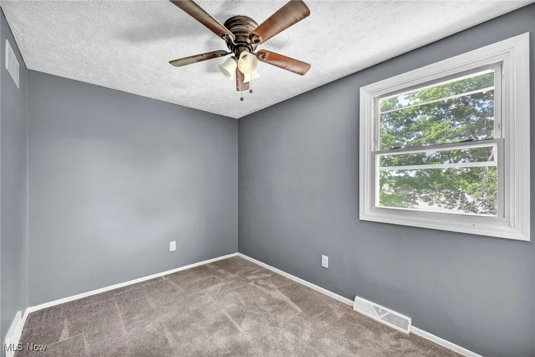 Carpeted empty room with ceiling fan and a textured ceiling