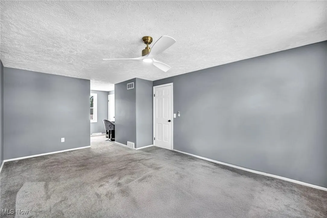 Carpeted spare room with a ceiling fan and a textured ceiling