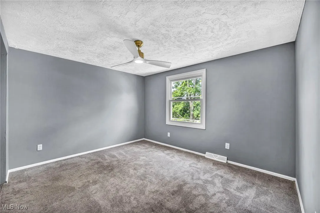 Carpeted spare room with ceiling fan and a textured ceiling