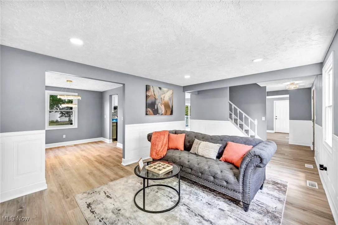 Living room with a textured ceiling, a wainscoted wall, stairway, light wood-style flooring, and recessed lighting