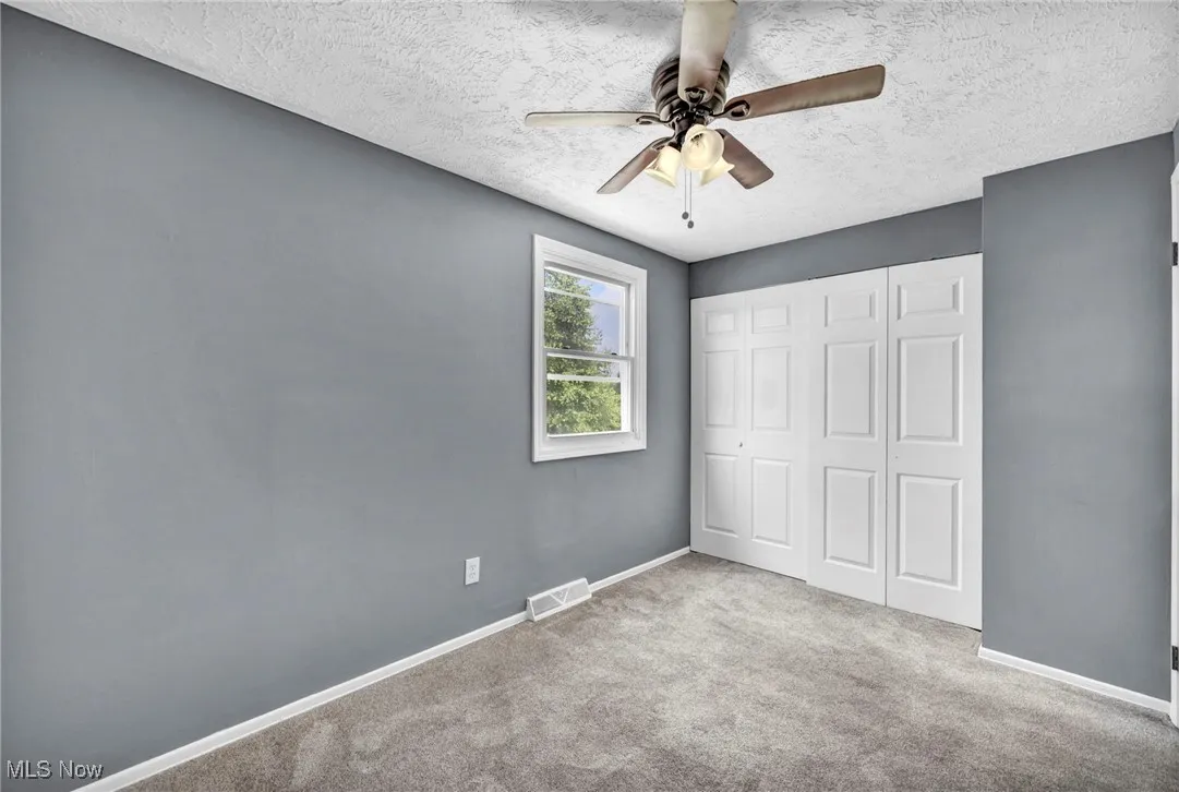 Unfurnished bedroom with a textured ceiling, carpet floors, a closet, and a ceiling fan