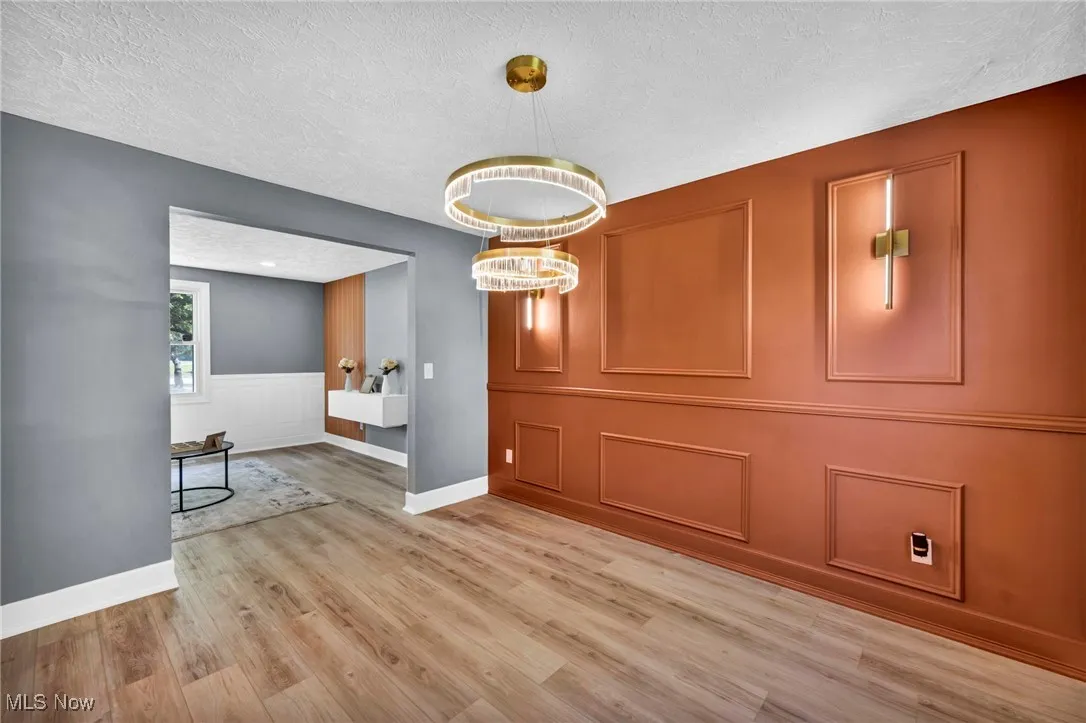 Unfurnished dining area featuring light wood-type flooring, a textured ceiling, a chandelier, a decorative wall, and wainscoting