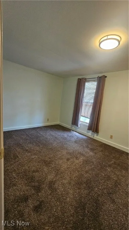 Spare room with dark carpet and baseboards
