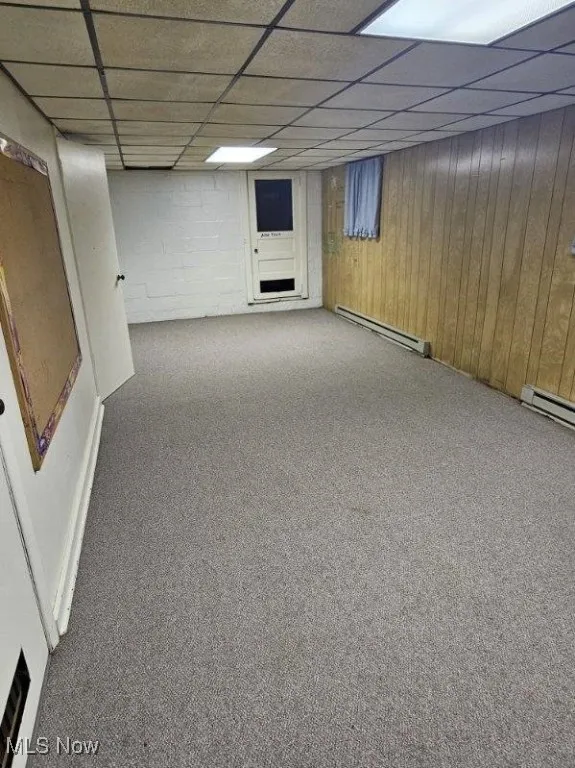 Finished below grade area with baseboard heating, carpet flooring, a drop ceiling, and wood walls