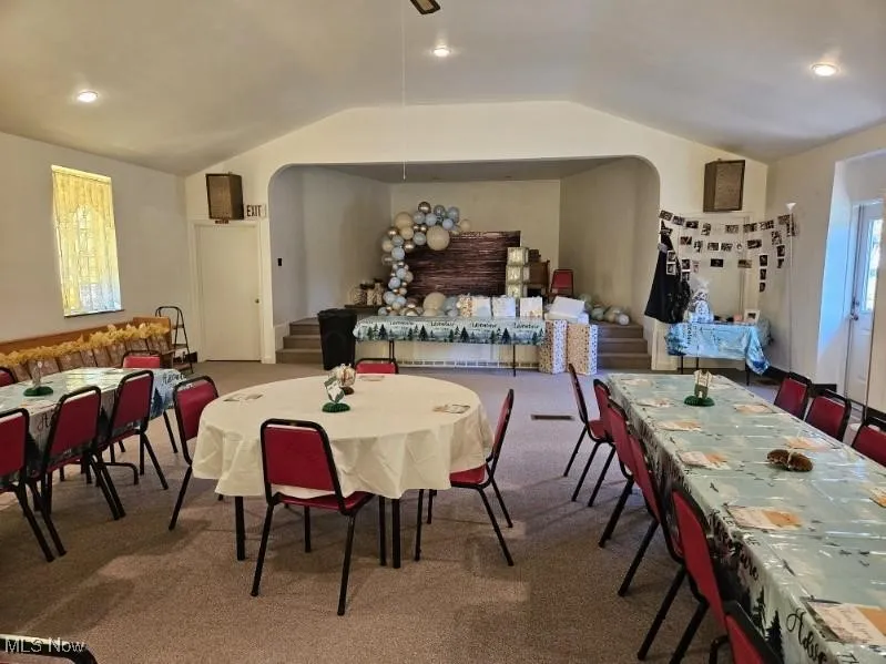 Dining area featuring lofted ceiling, carpet floors, stairway, and arched walkways