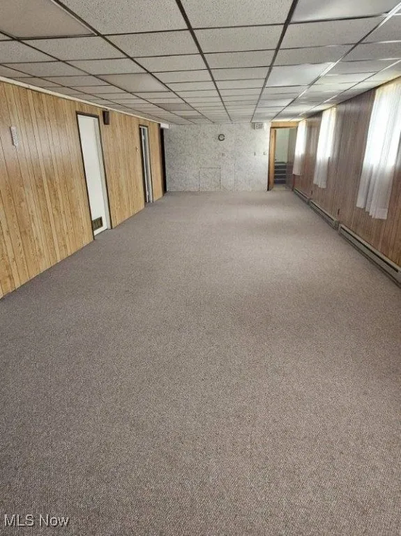 Carpeted spare room with wooden walls, a drop ceiling, and a baseboard radiator