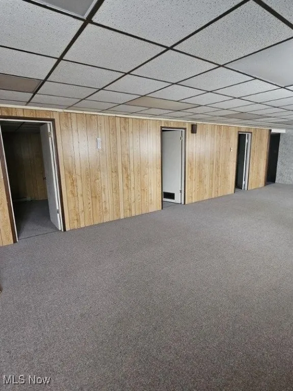 Finished basement with carpet flooring, a drop ceiling, and wood walls