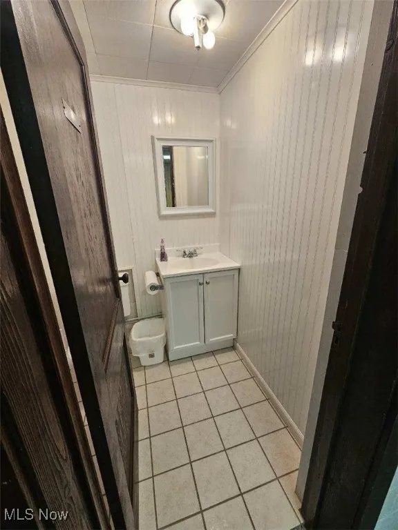 Half bathroom featuring vanity, tile patterned flooring, wood walls, and ornamental molding