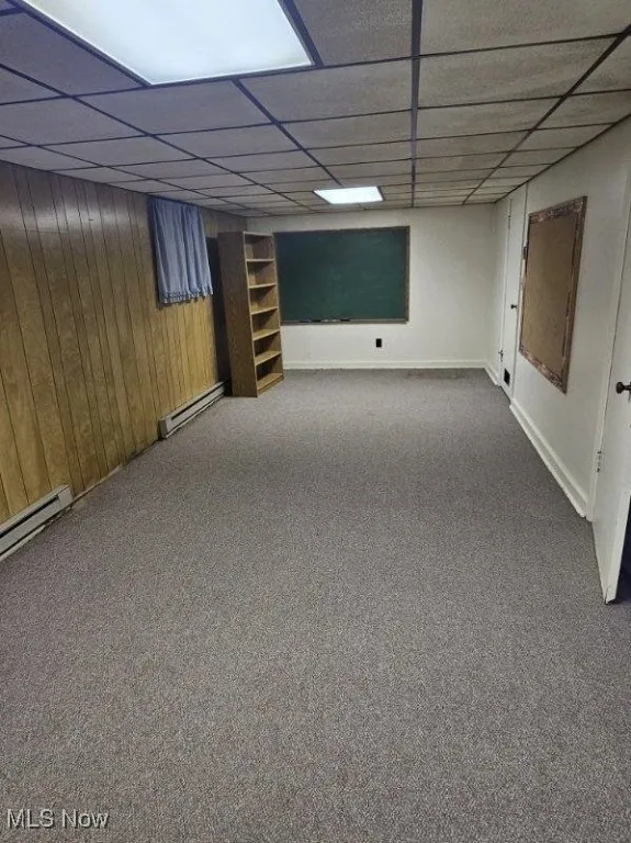 Finished basement featuring carpet, a baseboard radiator, a drop ceiling, and wooden walls