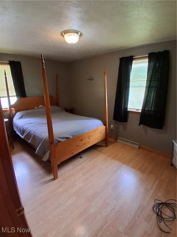 Bedroom with light wood-style flooring, a textured ceiling, and a baseboard heating unit