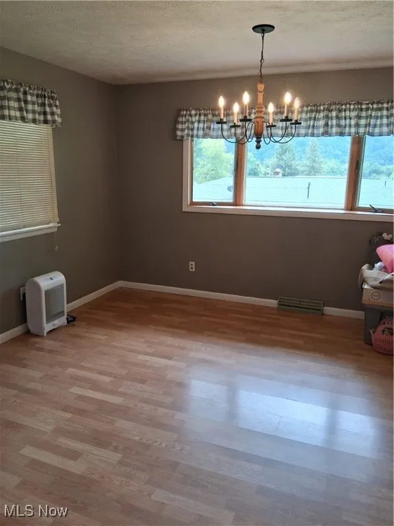 Unfurnished room featuring a chandelier, light wood finished floors, and a textured ceiling