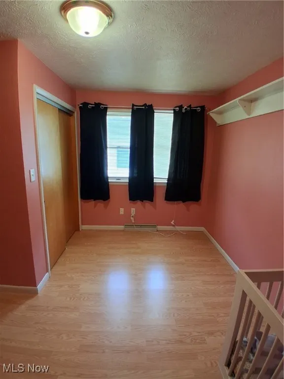 Unfurnished bedroom featuring light wood finished floors, a textured ceiling, and a closet