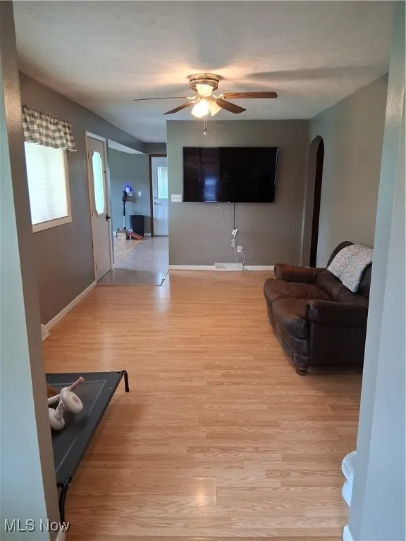 Living area featuring arched walkways, light wood-style flooring, and ceiling fan