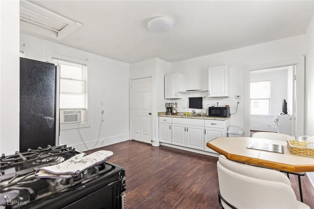 Kitchen featuring black appliances, dark wood-style flooring, white cabinets, and healthy amount of natural light