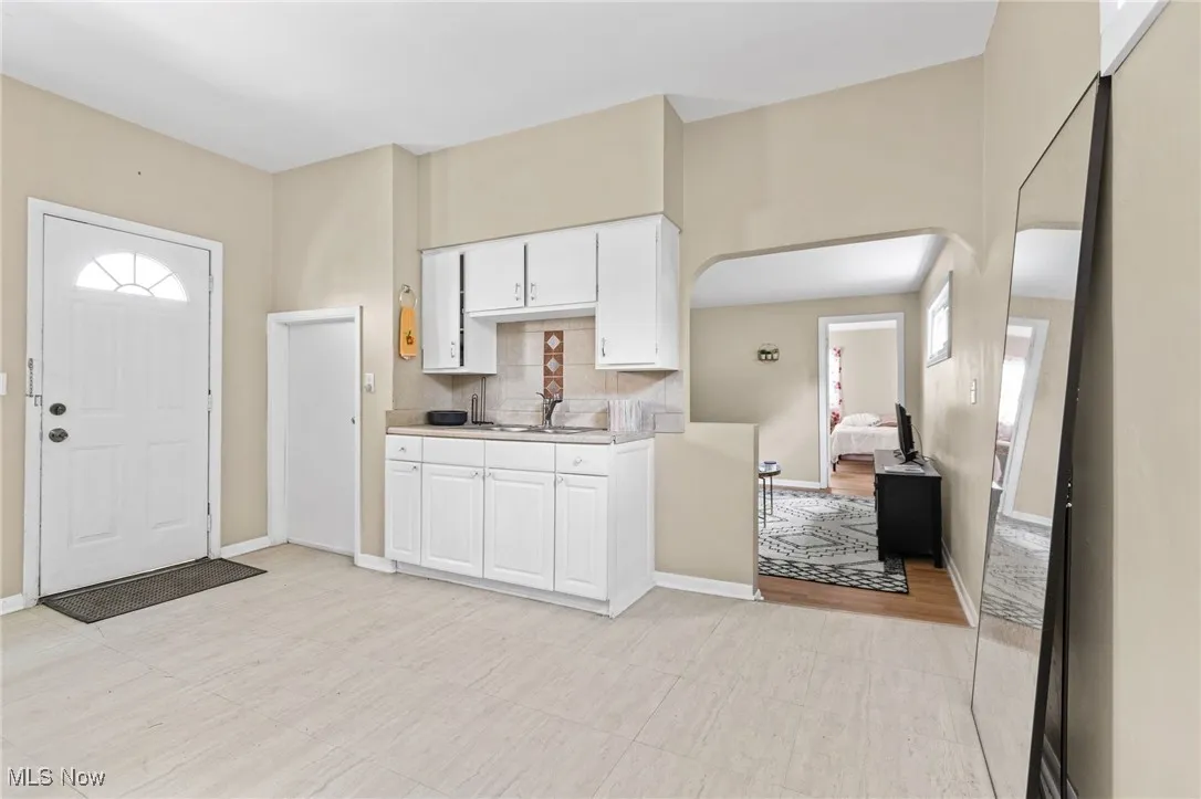 Kitchen featuring light countertops, backsplash, arched walkways, and white cabinetry