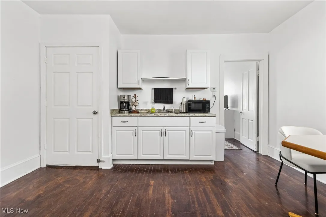 Kitchen featuring dark wood-style floors, white cabinets, light stone countertops, and black microwave