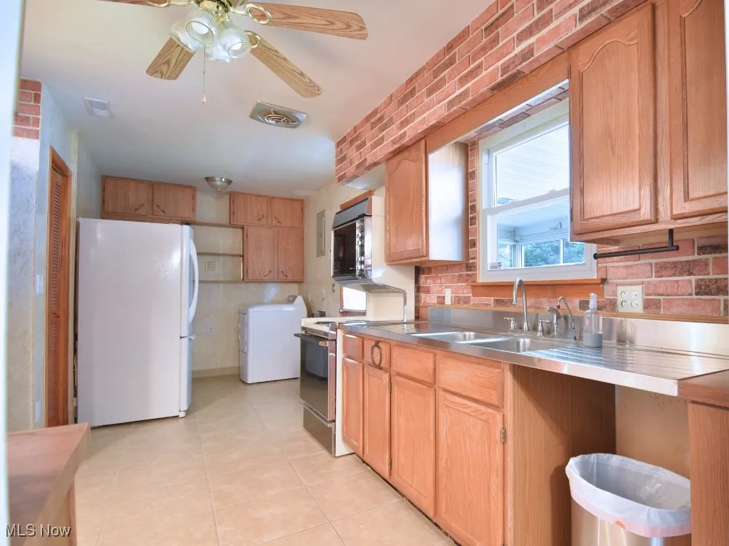 Kitchen freestanding refrigerator, electric range, washer / clothes dryer, light tile patterned flooring, and stainless steel countertops