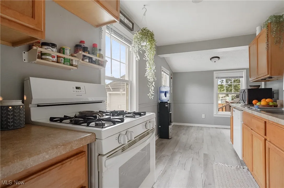 Kitchen featuring white appliances, lofted ceiling, and light wood-style floors