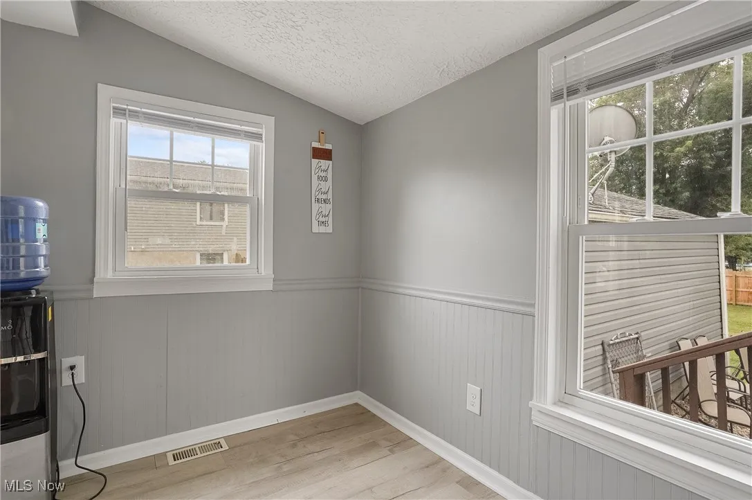 Empty room featuring lofted ceiling, wood finished floors, a textured ceiling, and wainscoting