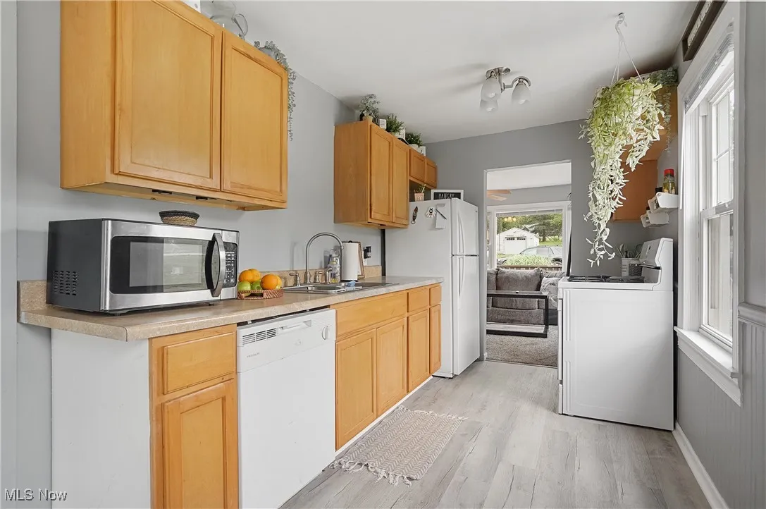 Kitchen with white appliances, light wood-style floors, light countertops, and light brown cabinetry