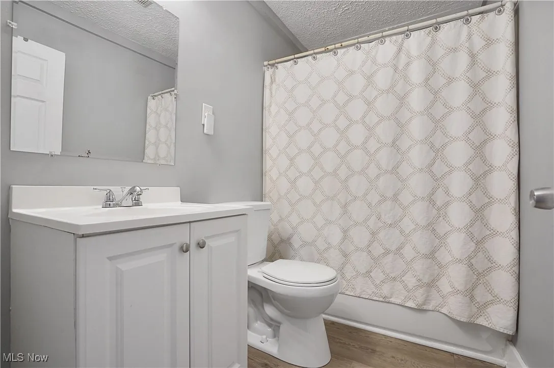 Bathroom with a textured ceiling, wood finished floors, vanity, and shower / tub combo