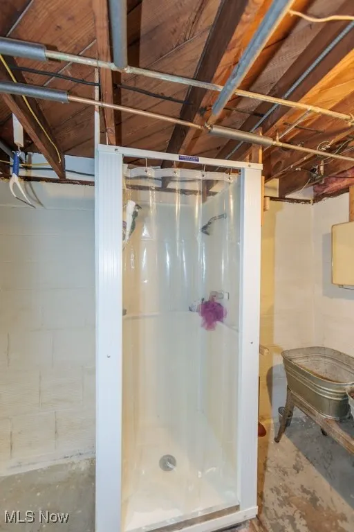 Bathroom with a stall shower, concrete block wall, and concrete floors